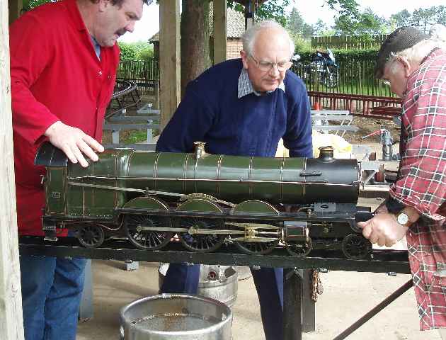 Three men working on a model steam locomotive on a raised outdoor track